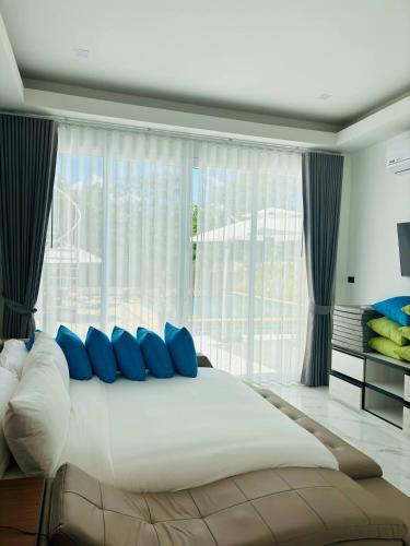 a large bed with blue pillows in front of a window at Baan Suan pool valley Villa in Ban Nong Thale