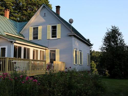 a blue house with a porch and flowers in the yard at Modern Luxury Farmhouse with a Jacuzzi Tub near Woodstock, Vermont in Bridgewater