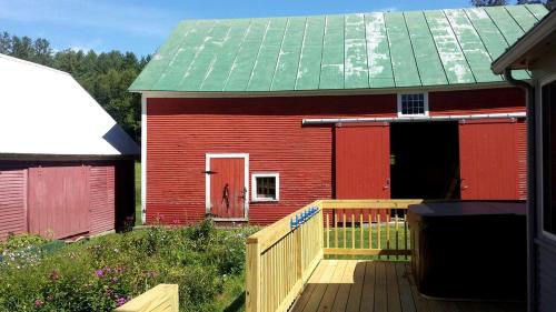 a red house with a green roof and a wooden deck at Modern Luxury Farmhouse with a Jacuzzi Tub near Woodstock, Vermont in Bridgewater