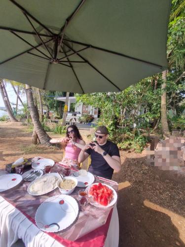 a man and woman sitting at a table under an umbrella at Green Island homestay in Kadalundi