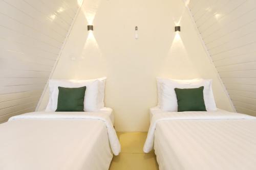 two beds in a room with white sheets and green pillows at Calma Resort at Megamendung, Bogor in Cilama