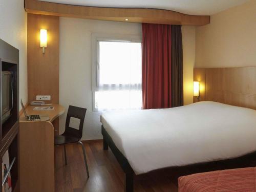 a hotel room with a bed and a desk and a bed and a window at ibis Beaune Centre in Beaune
