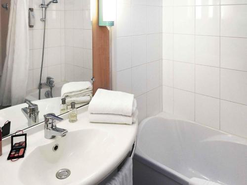 a white bathroom with a sink and a bath tub at ibis Beaune Centre in Beaune