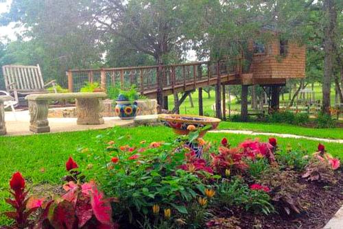 a garden with a deck and a bench and flowers at Romantic and Unique Tree House Rental on a Private Ranch in Central Texas in Waelder