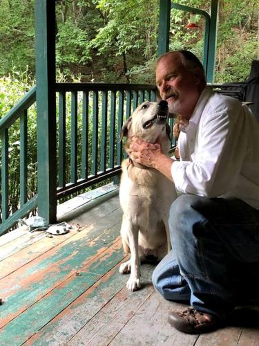 a man sitting on a porch with a dog at Unique Accommodation with Sauna for a Glamping Experience near Nantahala River, North Carolina in Marble