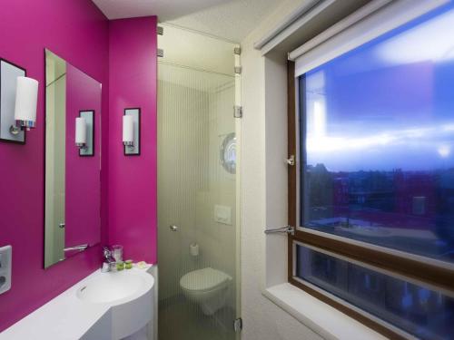 une salle de bain avec un mur rose, un lavabo et une fenêtre dans l'établissement ibis Styles Lille Centre Gare Beffroi, à Lille