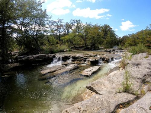 a river with a waterfall and rocks and trees at Beautiful Tented Cabin in Texas for Glamping by Guadalupe River in Hunt