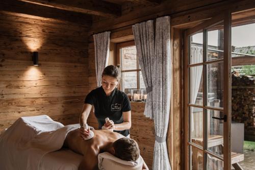 a woman is waxing a man lying on a bed at Alpzitt-Chalets in Burgberg