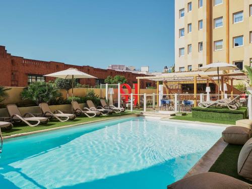 a swimming pool with chairs and umbrellas next to a building at ibis Nice Centre Gare in Nice