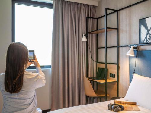 a woman taking a picture of a hotel room at ibis Paris CDG Airport in Roissy-en-France