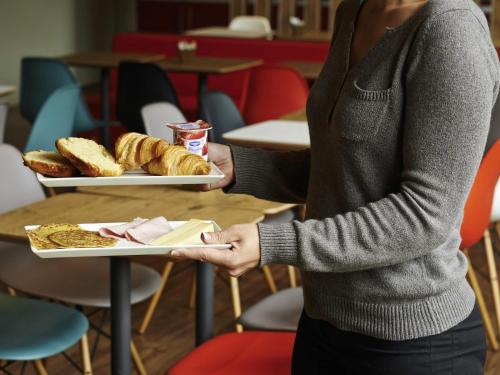 a woman holding two plates of food on a table at ibis Strasbourg Centre Historique in Strasbourg