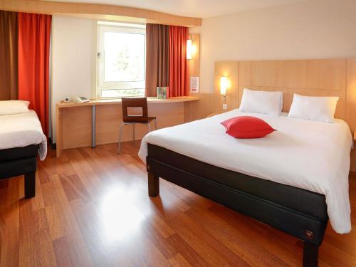 a hotel room with a large bed with a red pillow at ibis Toulouse Centre in Toulouse