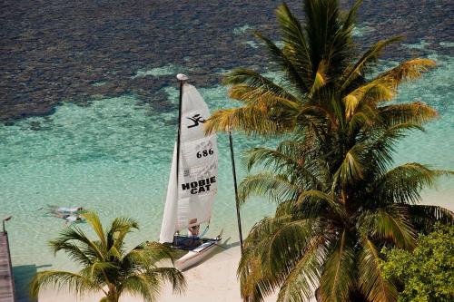 a sail boat on a beach with palm trees at Diamonds Athuruga Maldives Resort & Spa in Athuruga Island