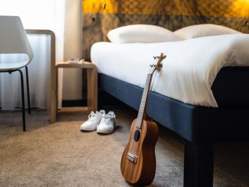 a guitar sitting on a bed next to a pair of shoes at ibis Gent Centrum Opera in Ghent