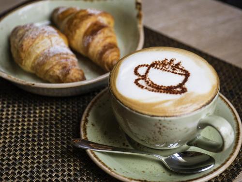 a cup of coffee next to a plate of croissants at ibis Gent Centrum Opera in Ghent