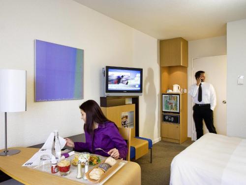 a woman sitting at a table in a hotel room at Novotel Marne-la-Vallée Noisy-le-Grand in Noisy-le-Grand