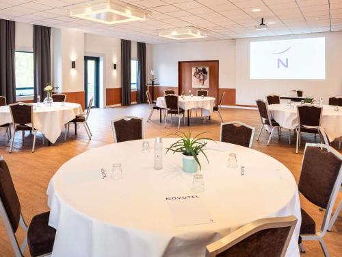 a conference room with tables and chairs and a screen at Novotel Marne-la-Vallée Noisy-le-Grand in Noisy-le-Grand