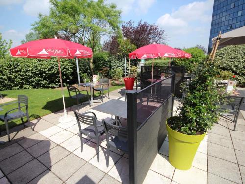 a patio with tables and chairs with red umbrellas at Ibis Marne la Vallée Noisy in Noisy-le-Grand