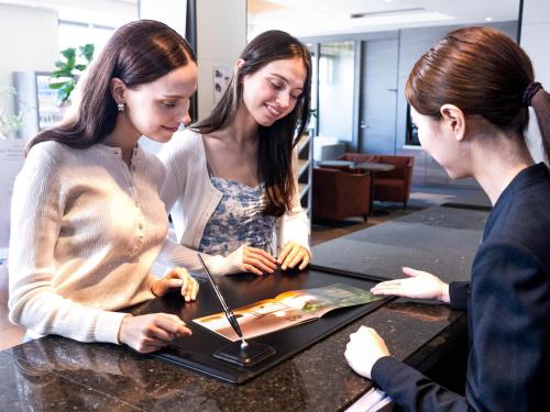 three women standing around a table with a laptop at Tokyu Stay Aoyama Premier in Tokyo