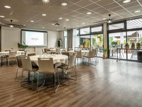 a dining room with tables and chairs and a projection screen at Mercure La Roche Sur Yon in La Roche-sur-Yon