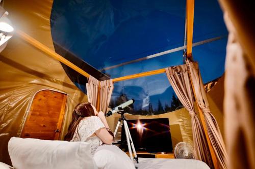 a woman is looking out a window with a camera at The X10 Nordic Tent and Glamping Pool Villa Khaoyai เขาใหญ่ - SHA Certified in Ban Thung Sawang
