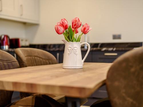 a white vase with red flowers on a wooden table at 2 Bed in Dalston 93820 in Dalston
