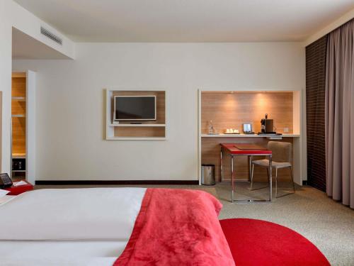 a bedroom with a bed and a desk and a television at Mercure Hotel Stuttgart Airport Messe in Stuttgart