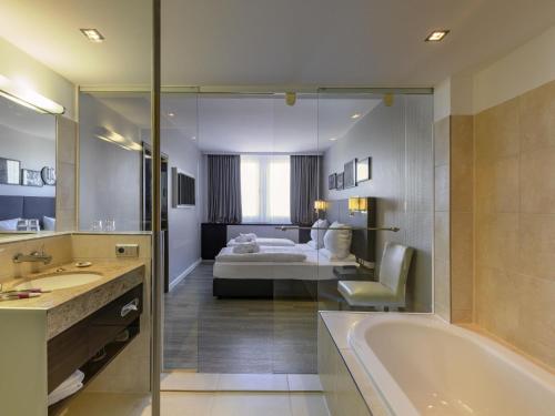 a bathroom with a tub and a bedroom with a bed at Mercure Hotel Potsdam City in Potsdam