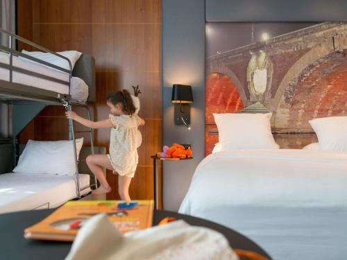 a little girl jumping on a bunk bed in a hotel room at Hotel Mercure Toulouse Centre Compans in Toulouse