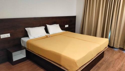 a bedroom with a large bed with yellow sheets and white pillows at Collection O Nandagokula Convention Centre Formerly Arasu Comforts in Hassan