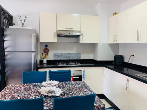 a kitchen with a table with blue chairs and white cabinets at Sunset Eden sea view in Aourir
