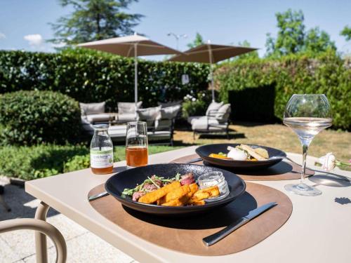 a table with two plates of food and a glass of wine at Mercure Compiègne Sud in Compiègne