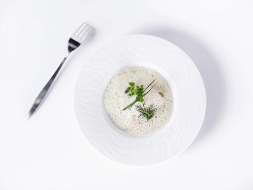 a white plate with a bowl of soup with a fork at Mercure Compiègne Sud in Compiègne