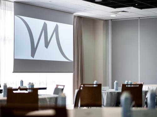 a conference room with tables and chairs and a large screen at Mercure Compiègne Sud in Compiègne