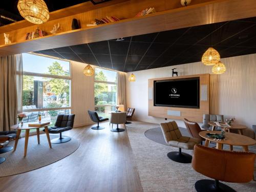 a waiting room with tables and chairs and a flat screen tv at Mercure Compiègne Sud in Compiègne