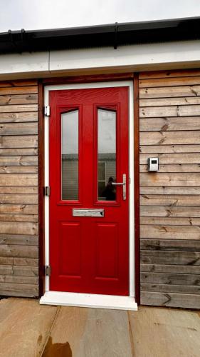 a red door on a wooden building with a person through it at Entick Lodge No 4 in Dunswell