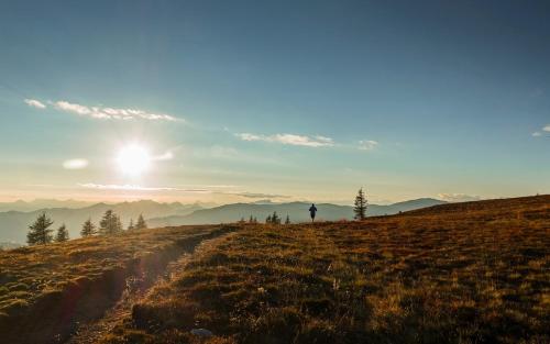 a person standing on a hill with the sun in the sky at Appartement Wolke7 byTILLY - Im Skigebiet Gerlitzen auf 1500m Seehöhe - familienfreundliche 3 Zimmer Wohnung - Hallenbad im Haus - moderne Küche mit Vollausstattung - Balkon - traumhafte Aussicht über ganz Kärnten - himmlisch bequeme Boxspringbetten in Treffen