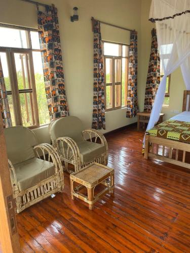 a bedroom with wicker chairs and a bed and wooden floors at Tabingi Safari Lodge in Katunguru