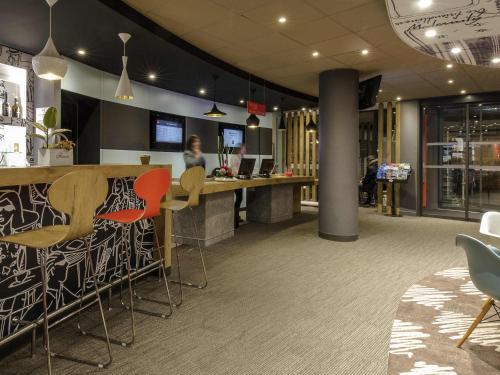 a restaurant with a bar with chairs and a woman at ibis Mulhouse Centre Filature in Mulhouse