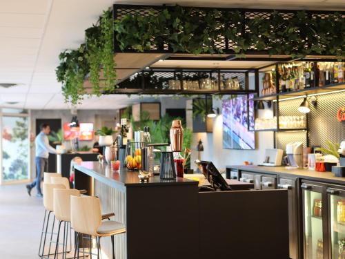 a restaurant with a bar with chairs and plants at ibis Aubenas in Aubenas