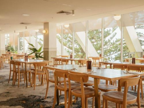 a restaurant with wooden tables and chairs and windows at Novotel Wollongong Northbeach in Wollongong