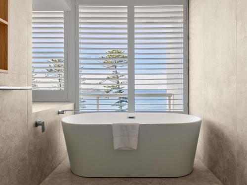 Una bañera blanca en un baño con ventana. en The Brighton Hotel Sydney - Mgallery Collection, en Sídney