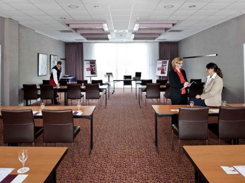 two women standing in a room with tables and chairs at Mercure Hotel Hamburg am Volkspark in Hamburg