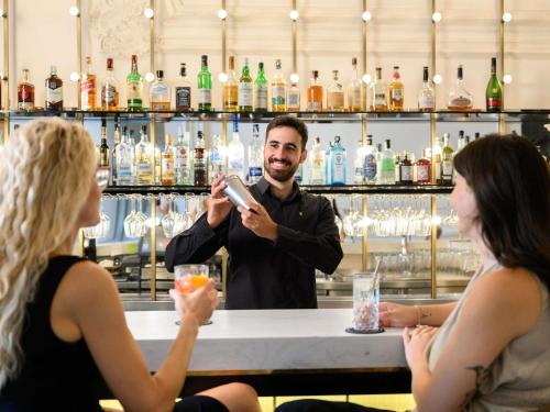 a man standing at a bar taking a picture of two women at Nemzeti Hotel Budapest - MGallery Collection in Budapest