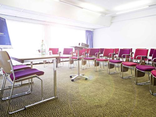 a room with purple chairs and tables and a screen at Novotel Genova City in Genova