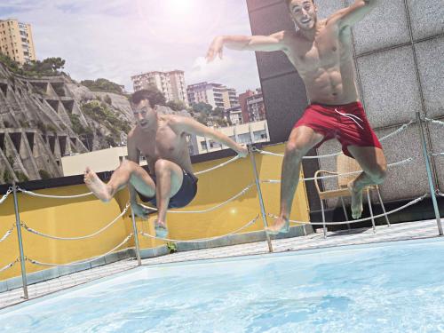 two men jumping off of a swimming pool at Novotel Genova City in Genova