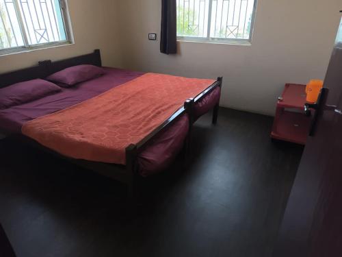a bedroom with a bed with a red comforter and two windows at Hill crest kodaikanal in Kodaikānāl