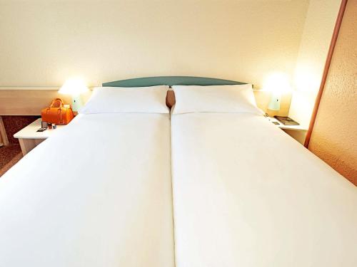 a large bed in a hotel room with two lamps at Hotel ibis Porto Sul Europarque in Santa Maria da Feira