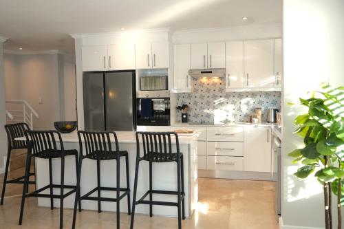 a kitchen with white cabinets and black bar stools at Modern Family Golf Lodge in Winelands Paradise in Paarl