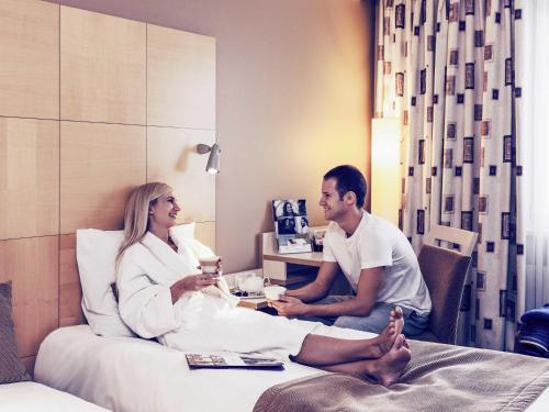 a man and woman sitting on a bed in a hotel room at Mercure Budapest Korona in Budapest